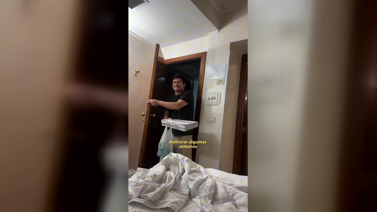 Red chegando na porta do apartamento com caixa de pizza e sacola de compras, na fase de recuperação